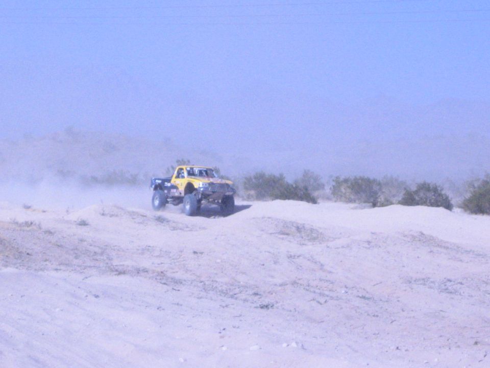 Yellow desert race truck on a sandy ridge with brush and dust
