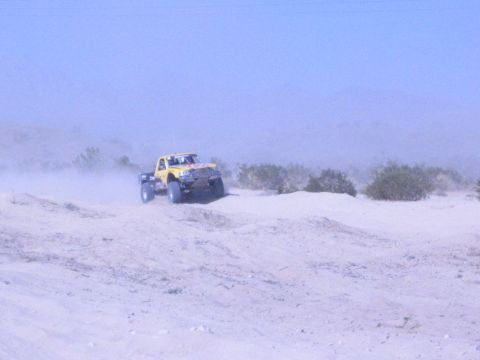 Yellow off-road truck driving over a sand berm in the desert