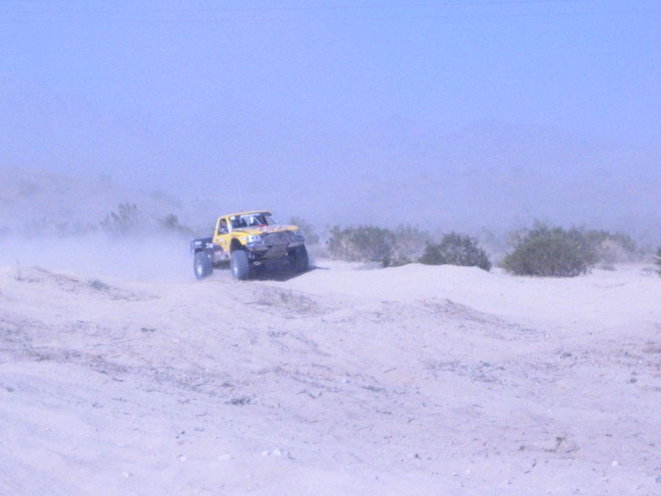 Yellow off-road truck driving over a sand berm in the desert