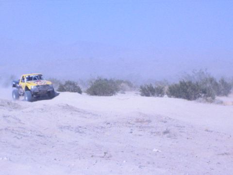 Yellow off-road race truck on sand at left of frame in desert