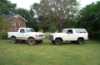 1988 Ford Bronco - Two white SUVs are parked side-by-side on a grassy lawn with trees in the background.