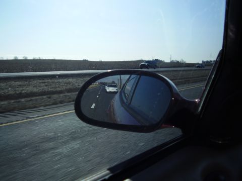 1997 Ford Taurus - A white sedan is seen in the side mirror while driving on a highway with other vehicles in the distance.
