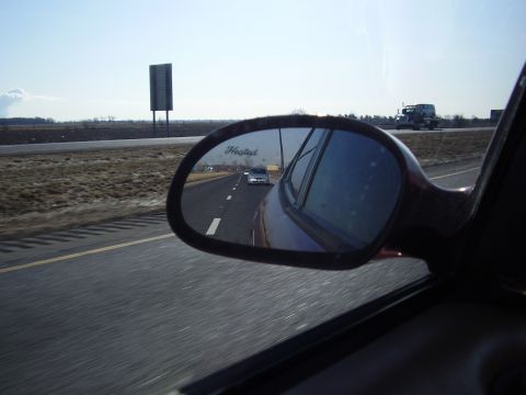 1997 Ford Taurus - Highway driving scene with a car reflected in the side mirror and a truck in the distance.