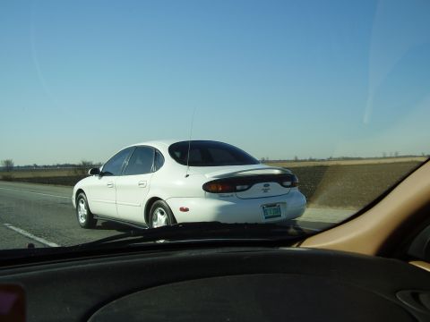 1997 Ford Taurus - A white sedan travels down a highway under a clear blue sky, with fields visible on the side.