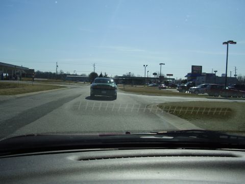 1997 Ford Taurus - A green 1997 Ford Taurus is seen from behind on a sunny day, with other vehicles and buildings in the background.