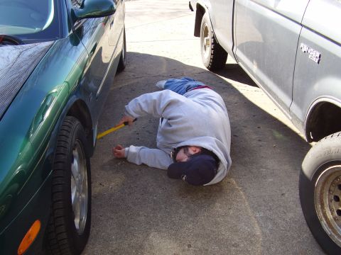 1997 Ford Taurus - A person is on the ground between a green car and a silver pickup truck, appearing to work on the green car's wheel.
