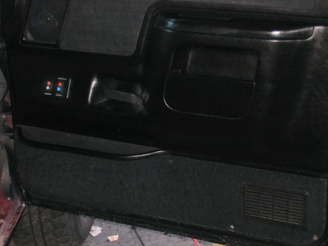 Black car door panel with a pull handle, storage pocket, and two toggle switches