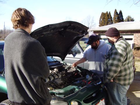 1997 Ford Taurus - Three men examine the engine bay of a green vehicle on a sunny day.