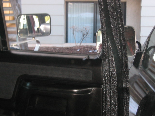 Black door panel with textured fabric insert and chrome handle, viewed from inside a vehicle