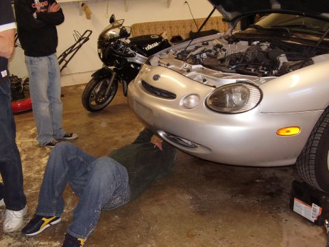 1997 Ford Taurus - A person works on a car in a garage while a motorcycle is parked nearby.