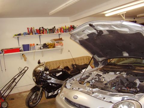 1997 Ford Taurus - A silver sedan's engine compartment is visible with the hood raised, parked indoors next to a black motorcycle.
