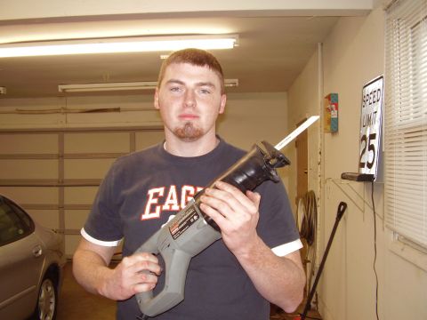 1997 Ford Taurus - A man stands in a garage holding a reciprocating saw, with a car visible to the left.