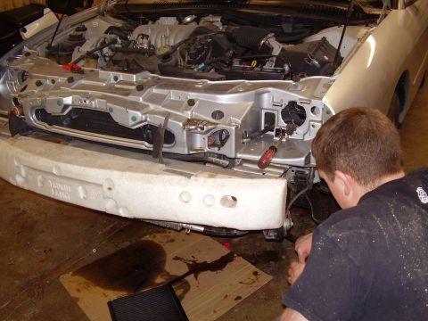 1997 Ford Taurus - Mechanic works on the front end of a 1997 Ford Taurus with the bumper removed.