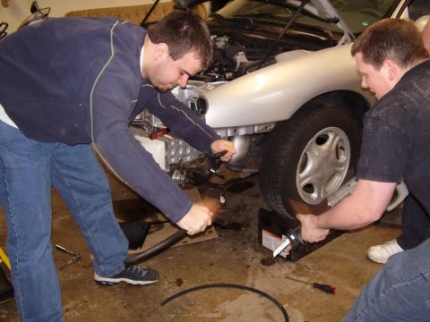 1997 Ford Taurus - Two men work on the front fender and wheel of a silver car.