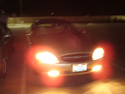 1997 Ford Taurus - A Ford Taurus is parked at night with its headlights illuminated, showing a partial view of another vehicle nearby.