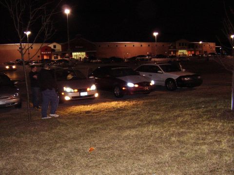 1997 Ford Taurus - A trio of sedans, including a 1997 Ford Taurus, are parked in a lot after dark.