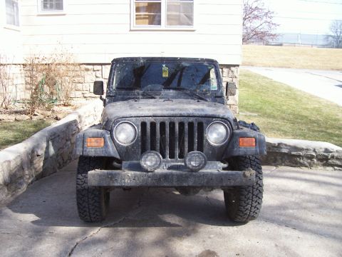 1998 Jeep TJ - A black Jeep Wrangler is parked in front of a house, showing its grille and headlights.
