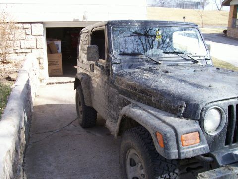 1998 Jeep TJ - This Jeep Wrangler is covered in mud, parked in front of a garage.