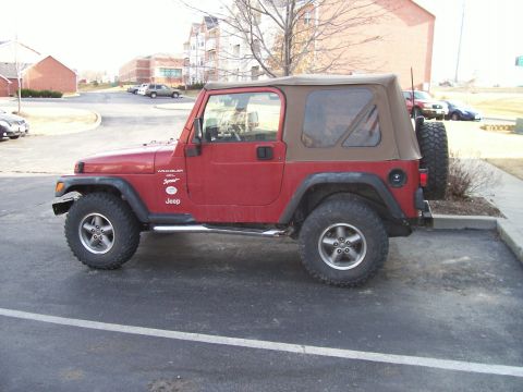 1998 Jeep TJ - A red Jeep Wrangler with a brown soft top is parked in a lot.