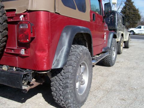 1998 Jeep TJ - A red Jeep Wrangler is parked in line with other vehicles, showing its rear side profile and off-road tires.