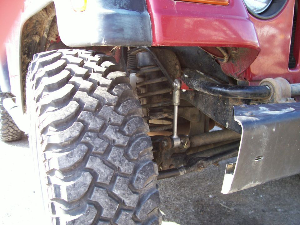 Close-up of a red Jeep's front tire and suspension system, showing off-road tires and lifted components