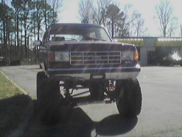 Dark Ford F-Series truck, lifted, front view. Grille has horizontal bars and a central Ford logo