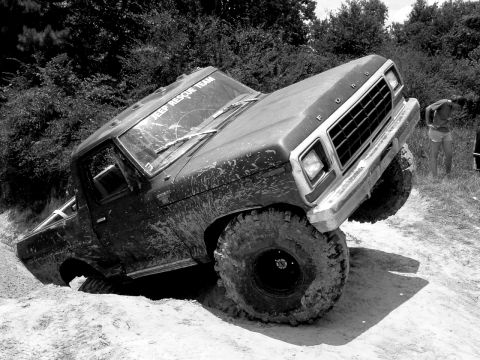 1993 Ford Bronco - This lifted Ford truck is stuck in the mud on an off-road trail, with a person visible in the background.