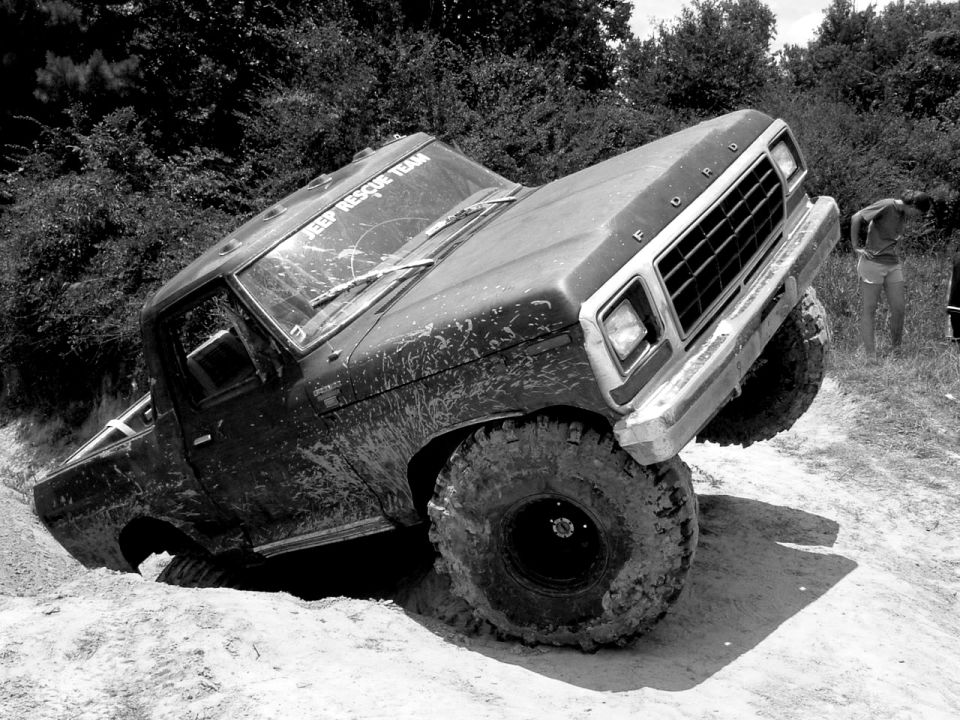 Muddy Ford F-Series truck stuck on a dirt hill. Text on windshield says 'JEEP RESCUE TEAM'