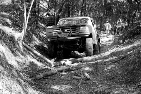 1993 Ford Bronco - A modified Ford F-Series truck navigates a challenging off-road path in a forest.