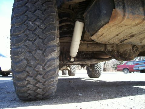 1998 Jeep TJ - Close-up of the undercarriage and suspension system on a modified Jeep TJ, with other cars parked nearby.