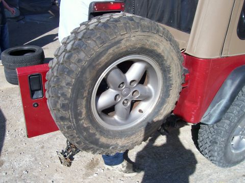 1998 Jeep TJ - The rear of a red Jeep Wrangler is shown with a spare tire mounted on the carrier and the driver's side door open.