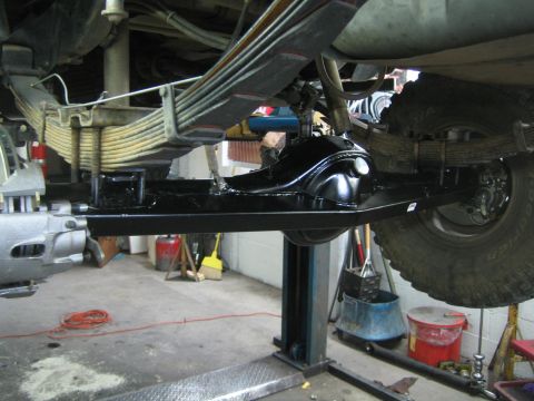 1990 Ford Bronco - Underside view of a truck on a shop lift showing a black rear axle, leaf springs and driveshaft.