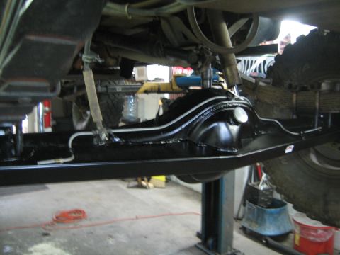 1990 Ford Bronco - Close-up underbody shot of a freshly painted black rear axle and leaf-spring suspension on a lift.