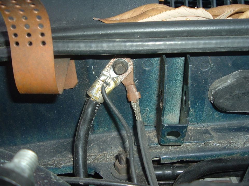 close-up of car battery cables connected to terminals, with some leaves on top