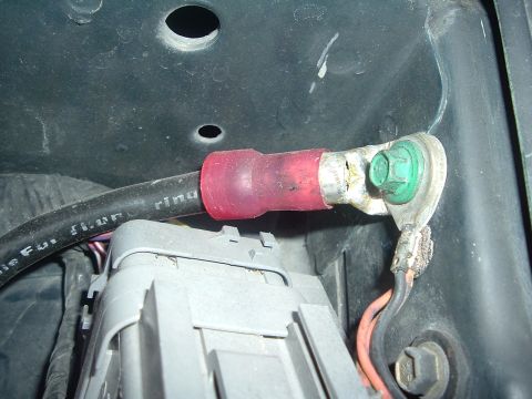 1993 Ford Taurus - Close-up of a battery cable connection with a red boot and a green bolt securing it to the terminal.
