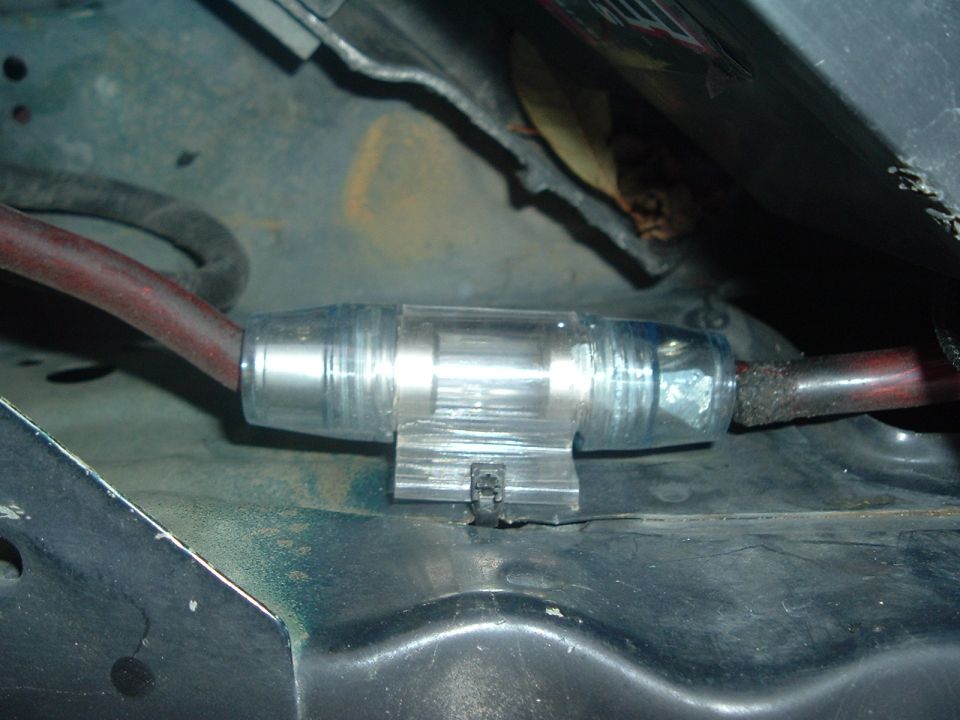 Inline fuse holder with a red wire connected to one end, mounted in a vehicle's engine bay