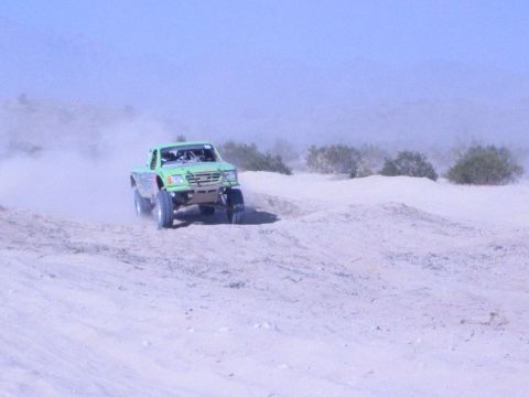 Green off-road race truck driving over a sand berm in the desert