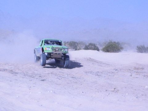 Green tube-chassis off-road race truck on a desert sand course