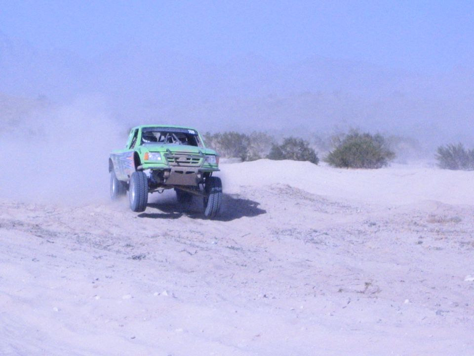 Green tube-chassis off-road race truck on a desert sand course