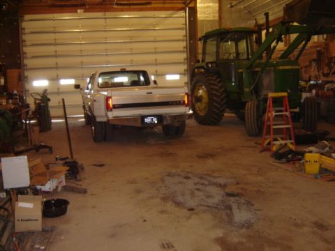 1992 Ford Bronco - A white Ford dually pickup truck and a green John Deere tractor are parked inside a garage with the large overhead door open.