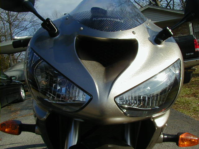 2006 Kawasaki Ninja front view showing headlights and fairing. A black car is parked to the left