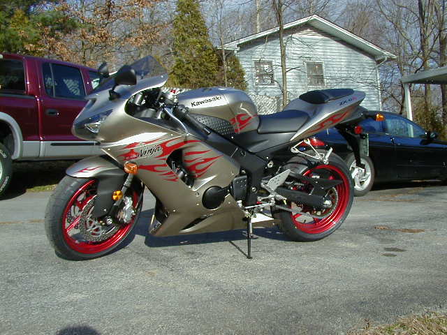 Gold Kawasaki Ninja motorcycle with red flame decals parked next to a red pickup truck and a black car