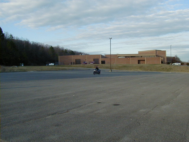 Motorcycle in a large, empty asphalt lot with a brick building in the background