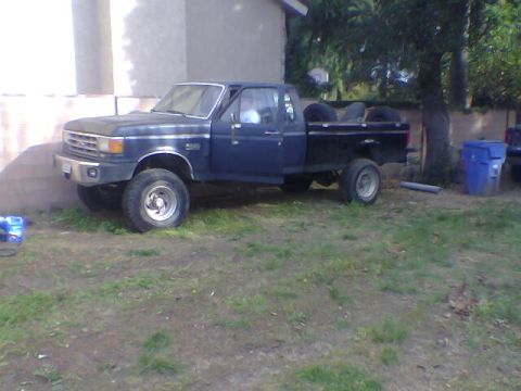 1987 Ford F-250 - This 1987 Ford F-250 pickup truck is parked on a grassy area next to a building and a tree.