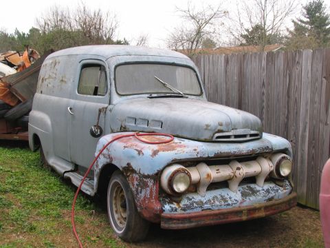 1952 Ford Panel Van - A weathered panel van sits in a yard, showing signs of age and disrepair.