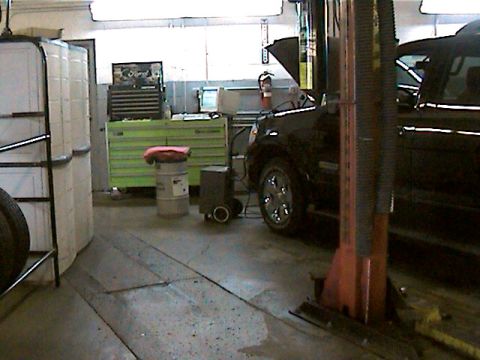 1977 Ford F-150 - A black SUV is parked inside a garage with its hood open, surrounded by various tools and storage containers.