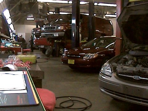 1977 Ford F-150 - An auto shop scene with multiple vehicles undergoing service, including a truck on a lift and cars in bays.