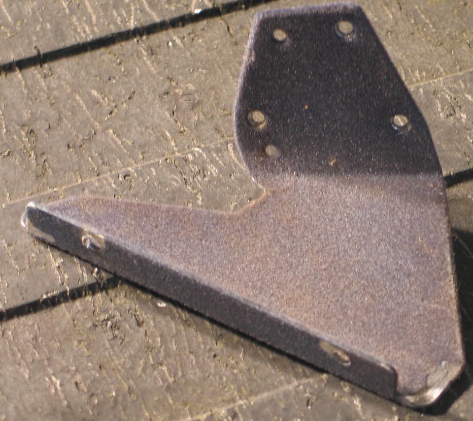 Metal bracket with four holes on top and two on the side, resting on a wooden surface