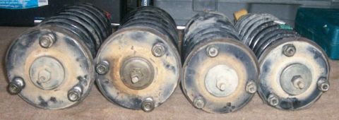 1993 Ford Bronco - Four used coil-over strut assemblies stood on end and photographed from the top-mount end, showing their three-stud mounting plates, center…