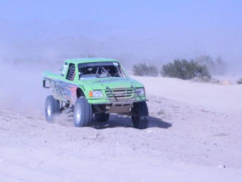Green number-708 off-road race truck airborne over a sand dune